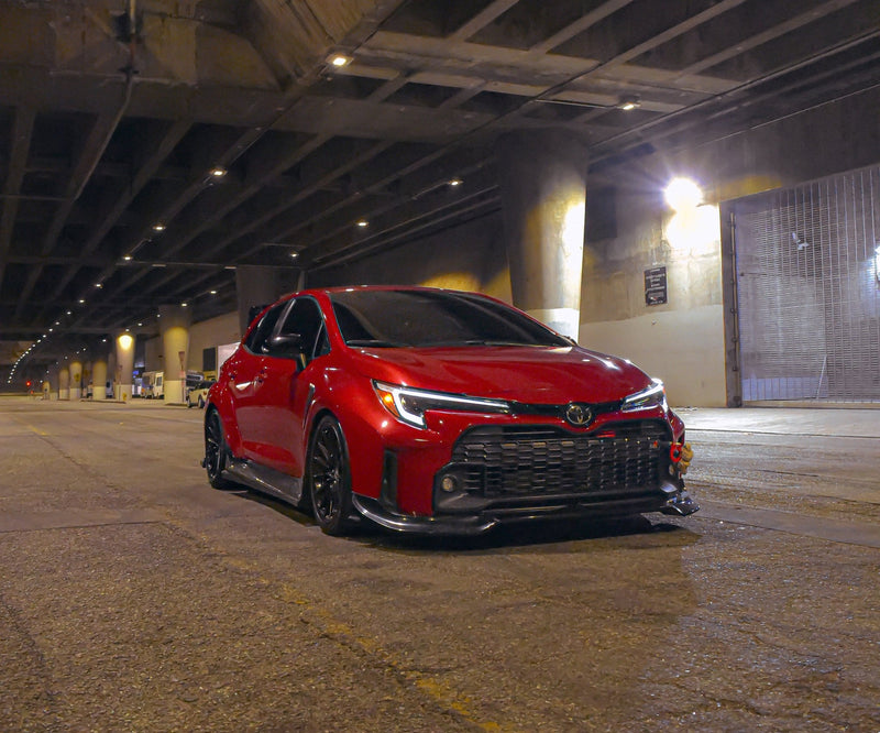 Load image into Gallery viewer, Gloss black V2 front lip installed on a red Toyota GR Corolla E210 (2023-2024) parked under a bridge.