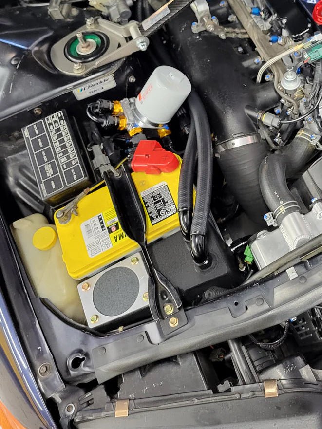 Load image into Gallery viewer, SynGarage black oil separator catch can system installed in a Nissan R32 GTR engine bay with yellow battery.