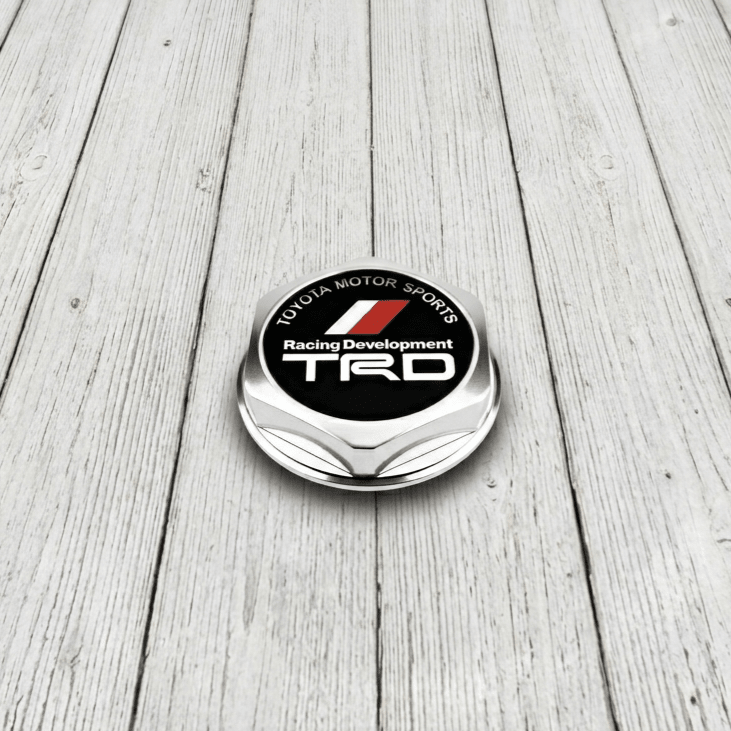 ギャラリービューアに画像をロードする, Genuine silver TRD engine oil cap for Toyota Supra MK4 with black and red racing logo on a light wood background.