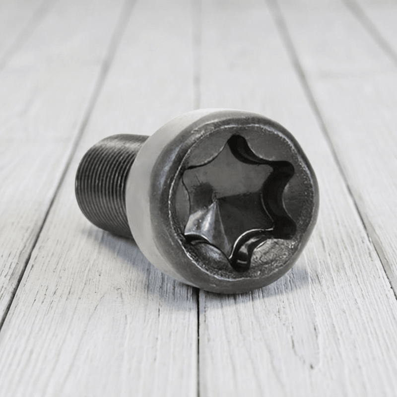 Load image into Gallery viewer, New black Nissan flywheel bolt with star-drive head, angled view on white wood background.