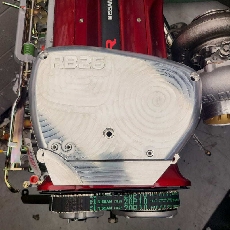 Load image into Gallery viewer, Silver billet aluminum RB26 engine front cover with machined swirl details installed on a red Nissan engine.