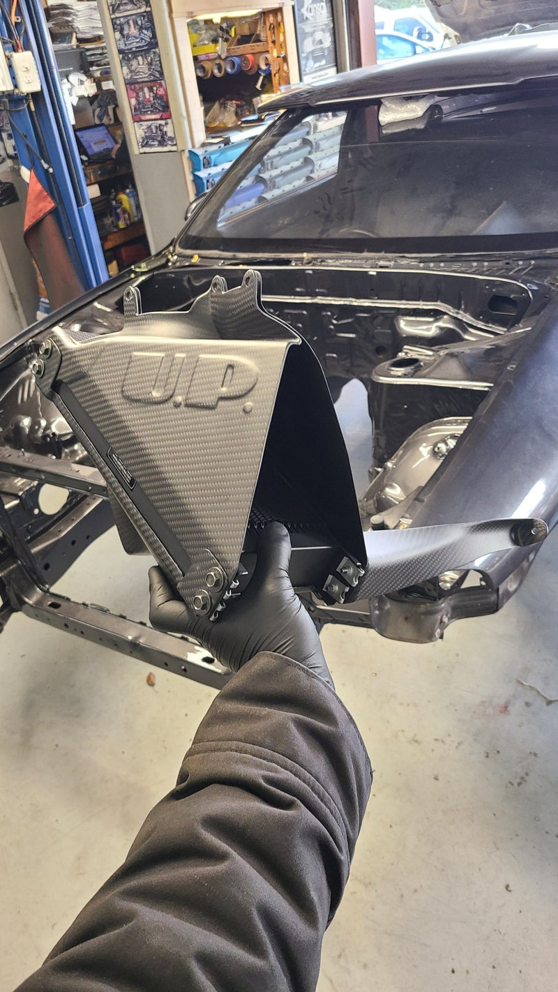 Load image into Gallery viewer, U.P.G oil cooler and carbon fiber duct combo for R32 GTR, held by a gloved hand in a workshop.