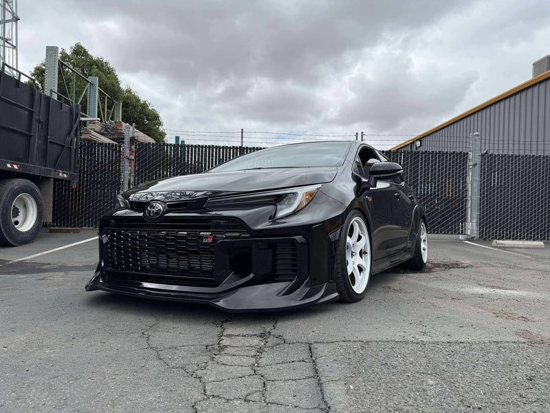 Load image into Gallery viewer, Gloss black front lip on a black 2025 Toyota GR Corolla (E210, Kouki) with white wheels parked in a lot.