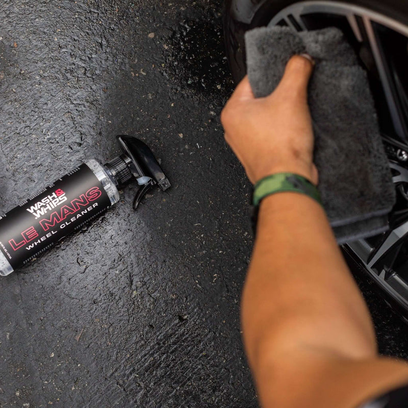 ギャラリービューアに画像をロードする, Wash & Whips Le Mans wheel cleaner bottle next to a hand using a grey microfiber towel to clean a car wheel.