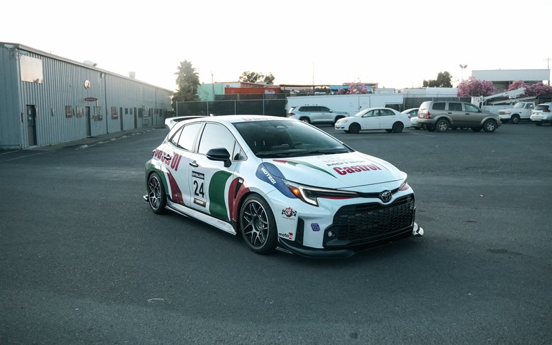 Load image into Gallery viewer, Black V2 front lip installed on a white 2023-2024 Toyota GR Corolla (E210) with Castrol racing livery.