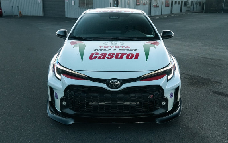 Load image into Gallery viewer, Black V2 front lip installed on a white 2023-2024 Toyota GR Corolla (E210) with Castrol livery.