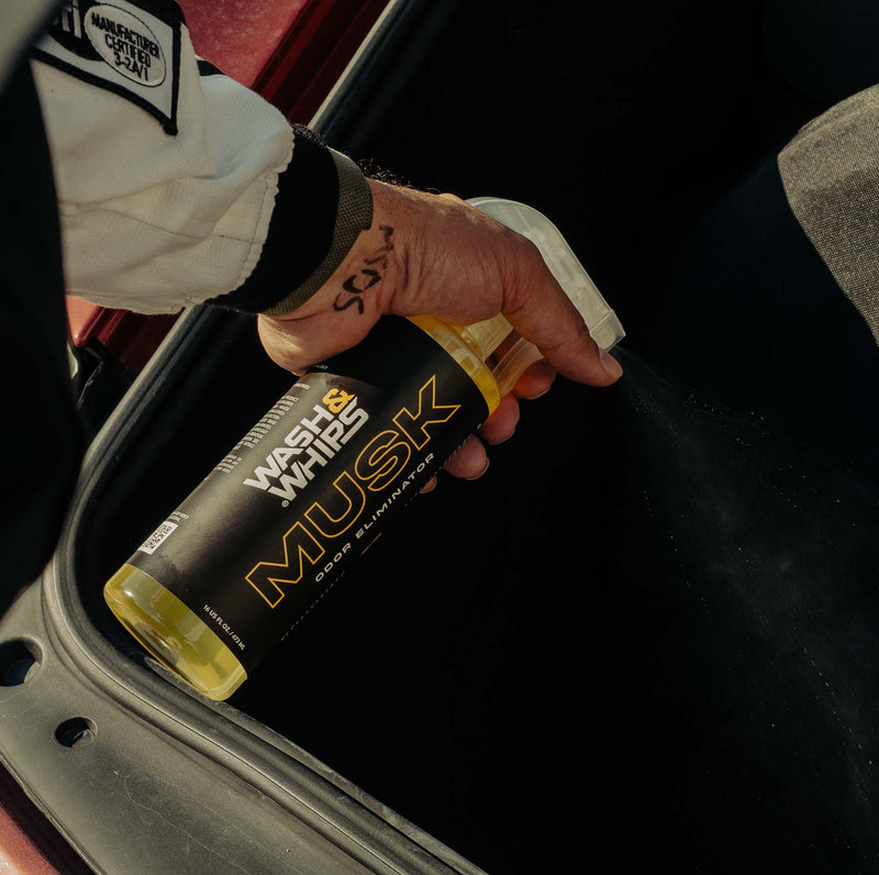 ギャラリービューアに画像をロードする, Hand spraying yellow Wash & Whips Musk odor eliminator into a dark car interior.