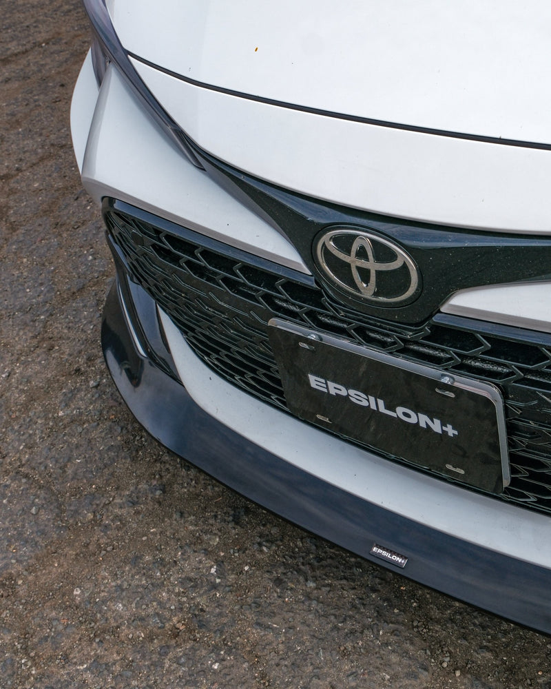 Load image into Gallery viewer, Gloss black front lip installed on a white 2023+ Toyota Corolla Hatchback (E210 Kouki) with Epsilon+ branding.