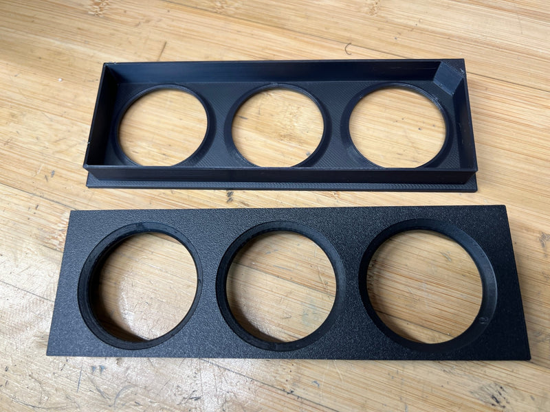 Load image into Gallery viewer, Black 3D-printed triple DIN gauge bezel for Nissan R32 Skyline, shown from front and back on a wooden surface.