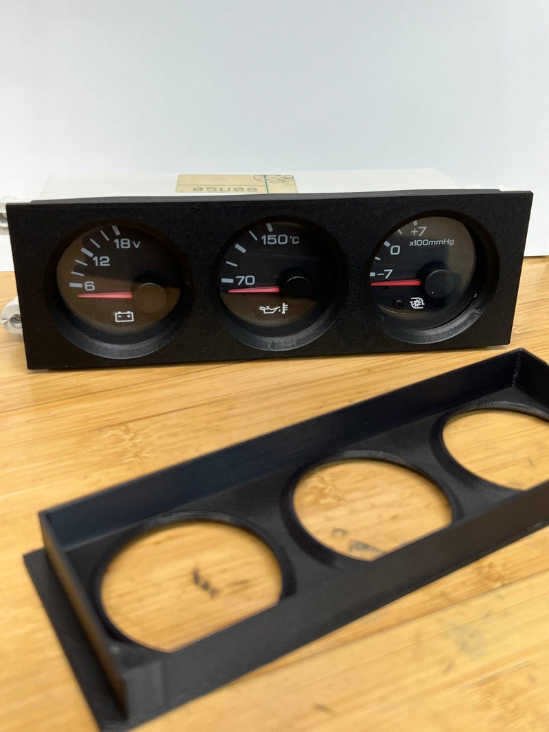 Load image into Gallery viewer, Black R32 Skyline triple DIN gauge cluster with gauges and a separate matching black 3D-printed bezel on a wood surface.