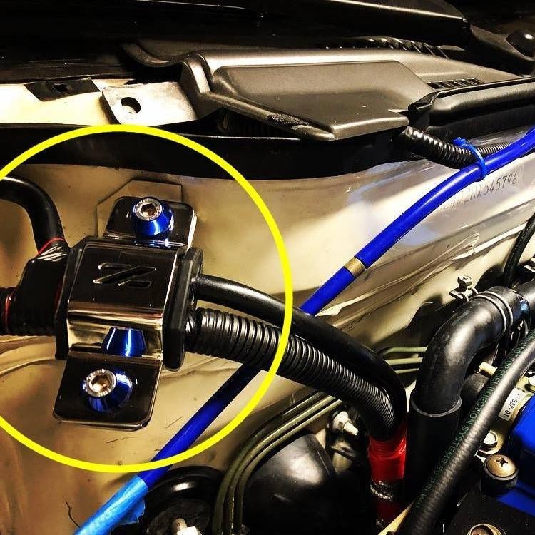 Load image into Gallery viewer, ZSPEC stainless steel silver battery cable bracket with blue bolts installed on a Nissan 300zx Z32 engine bay.