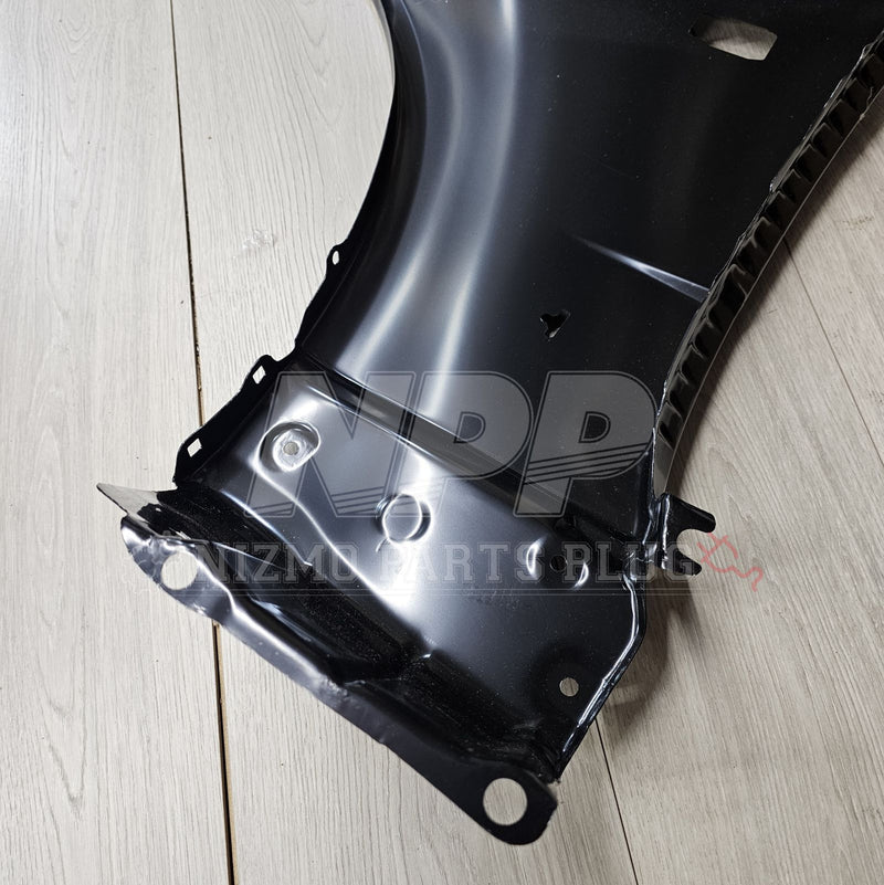 ギャラリービューアに画像をロードする, New black Nissan R34 Skyline GTR right-hand front fender assembly on a wood floor background.
