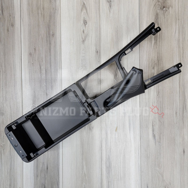 Load image into Gallery viewer, Black Nissan R34 Skyline center console trim with integrated handbrake boot on a light wood background.