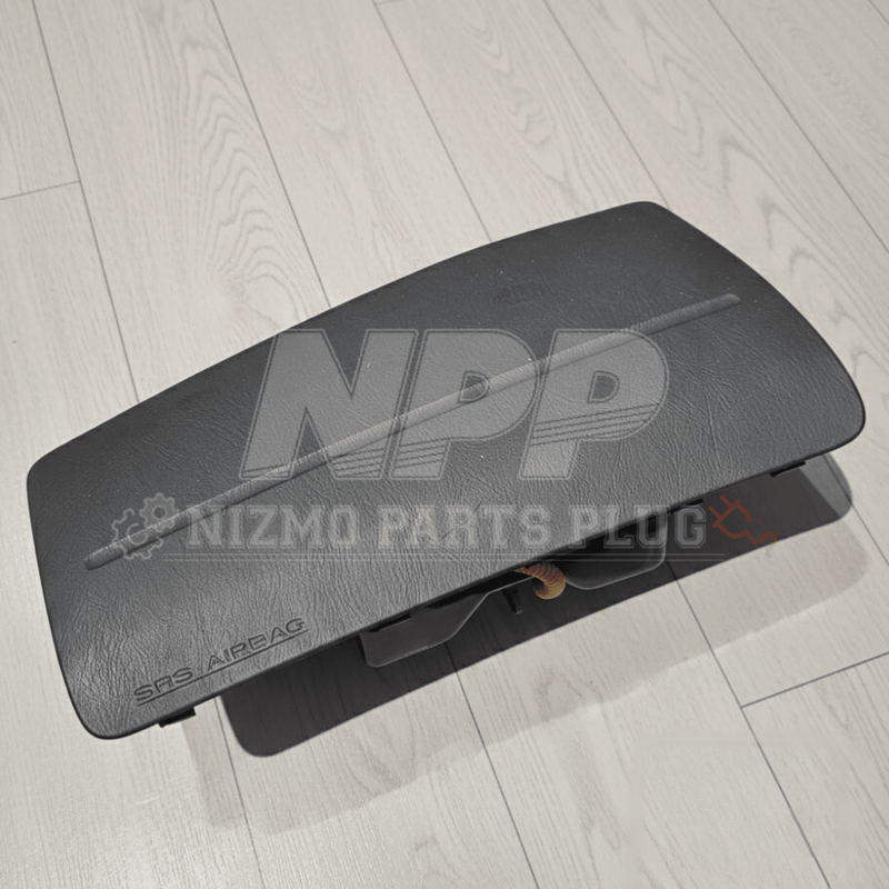 Load image into Gallery viewer, Black Nissan R34 Skyline passenger side SRS airbag assembly in good condition on a light wood floor.