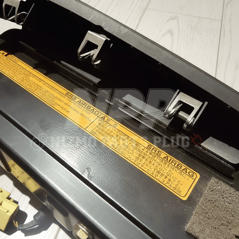 Load image into Gallery viewer, Black Nissan R34 Skyline passenger SRS airbag assembly with yellow warning label, viewed from the rear.
