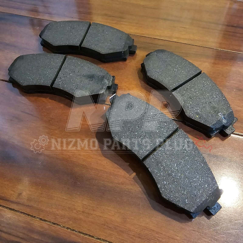 Load image into Gallery viewer, New Nissan S14 240SX OEM black front brake pad set displayed on a wooden surface.