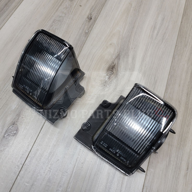 Load image into Gallery viewer, Pair of smoke-tinted Nissan R32 Skyline Coupe reverse light assemblies on a wooden background.