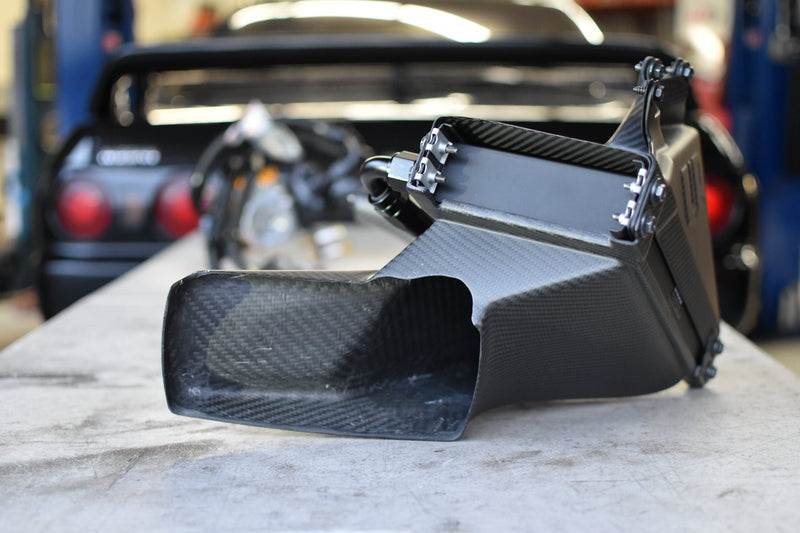 Load image into Gallery viewer, U.P.G. oil cooler with carbon fiber ducting for R32 GTR, shown on a workbench with a blurred R32 in the background.