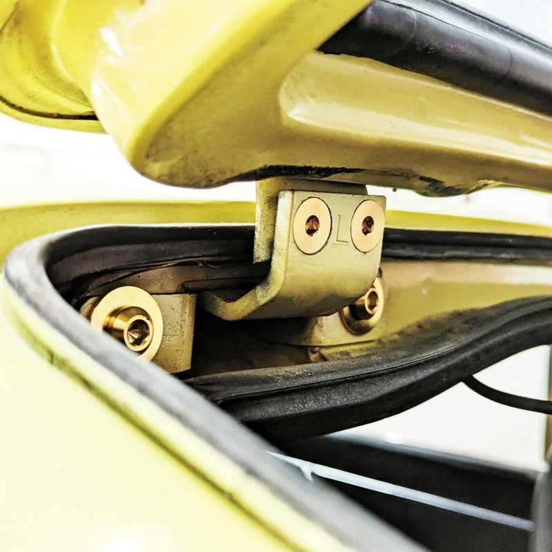 Load image into Gallery viewer, ZSPEC titanium fastener kit installed on a Datsun S30 hatch hinge, featuring gold-toned bolts on a yellow body.