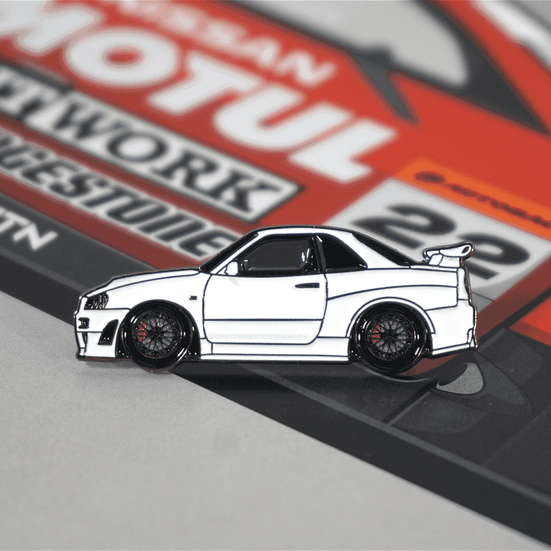 Load image into Gallery viewer, White Nissan Skyline R34 GT-R enamel pin with black wheels, shown against a red Motul racing livery background.