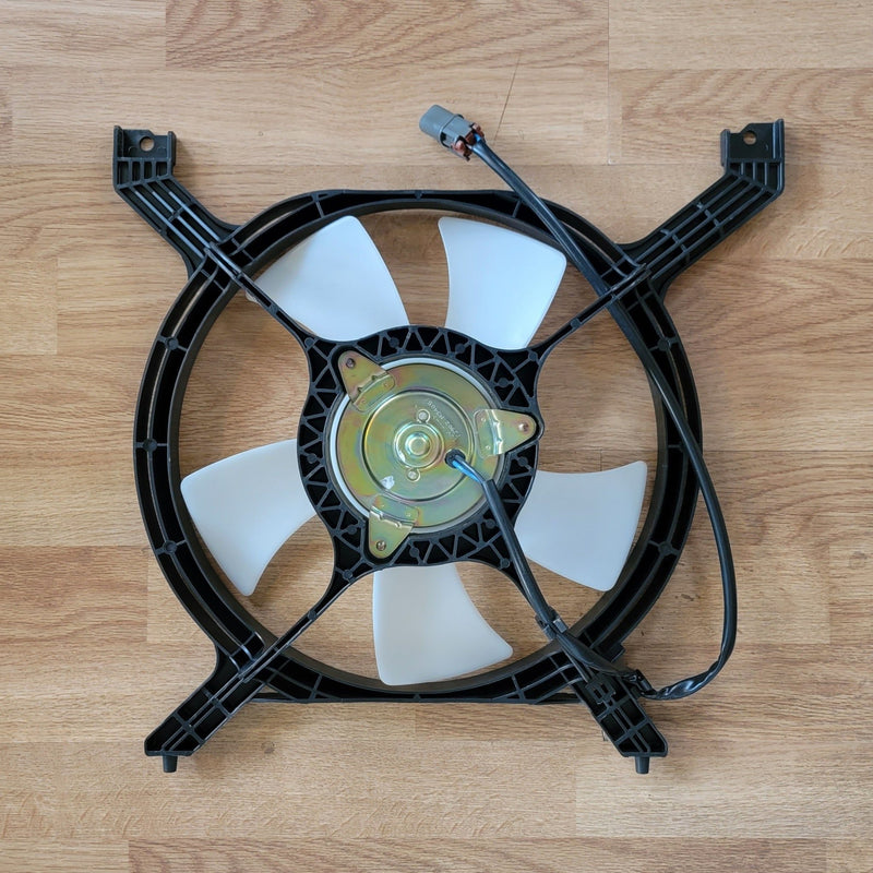 Load image into Gallery viewer, NOS S13 240SX A/C condenser fan with black shroud, white blades, and gold motor housing on a wooden surface.