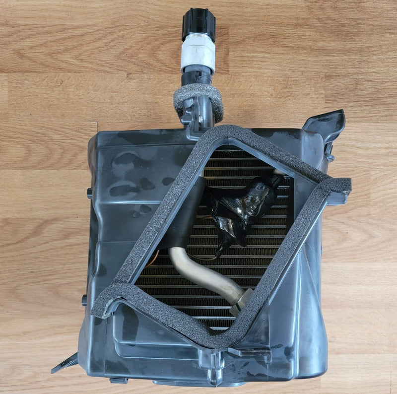 Load image into Gallery viewer, N.O.S. S13 240SX R134A A/C evaporator unit in black plastic with foam seals on a wooden background.