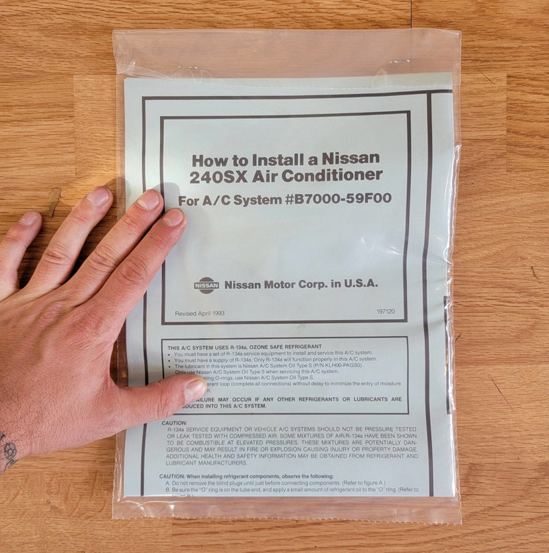 Load image into Gallery viewer, N.O.S. S13 240SX R134A A/C installation manual in a sealed plastic bag held by a hand.