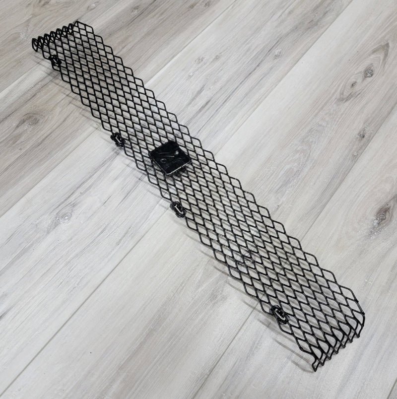 Load image into Gallery viewer, Black metal mesh upper front bumper grill for Nissan R34 Skyline GTR on a light wood grain background.