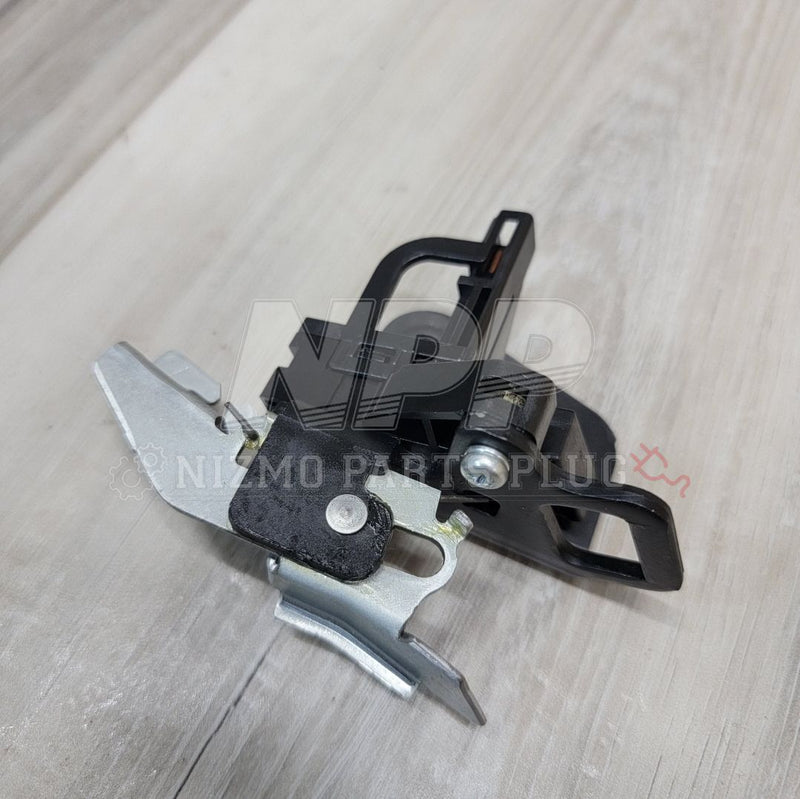 Load image into Gallery viewer, Nissan R34 Skyline trunk latch striker assembly with black plastic and silver metal components on a wood surface.