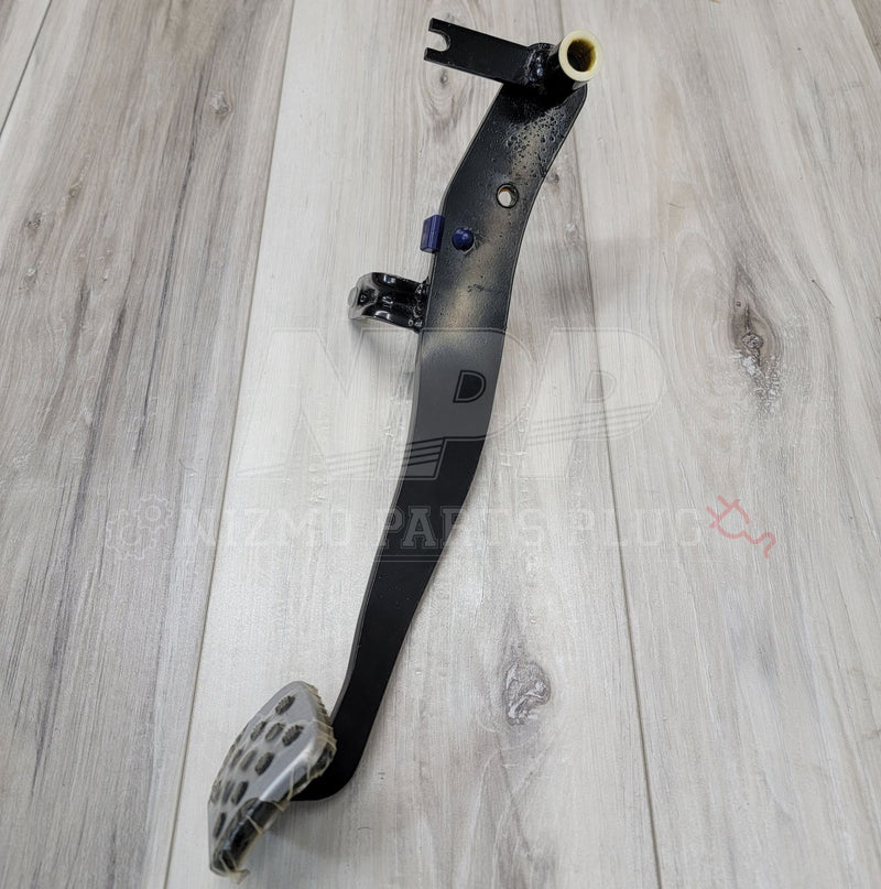 Load image into Gallery viewer, Black metal Nissan R34 Skyline GT-R clutch pedal arm assembly with silver pedal pad on a wood floor background.