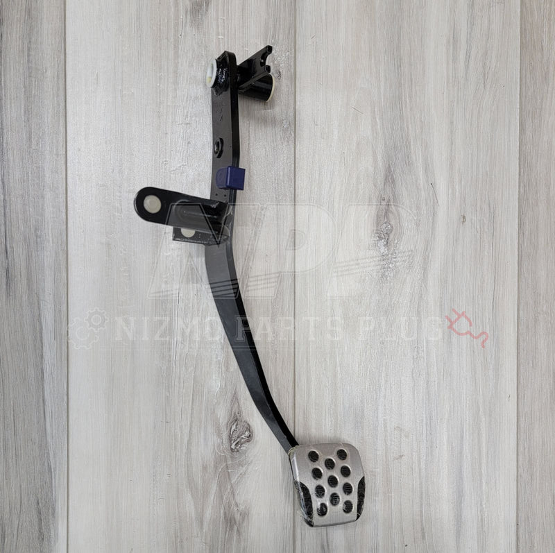Load image into Gallery viewer, Black Nissan R34 Skyline GT-R clutch pedal arm assembly with silver drilled pedal pad on a wood background.