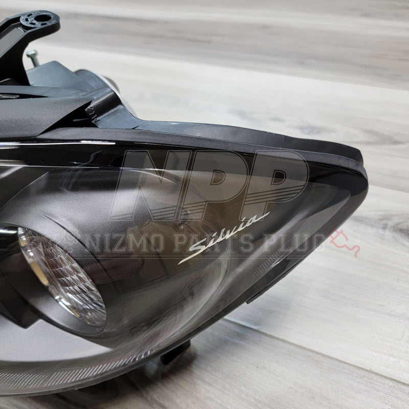Load image into Gallery viewer, OEM Nissan S15 Silvia HID headlight assembly featuring a black housing and iconic "Silvia" script on the lens.