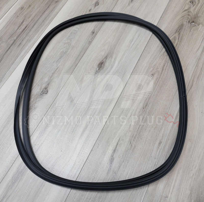 Load image into Gallery viewer, Black rubber rear windshield molding for Nissan R34 Skyline coupe, coiled on a wood background.