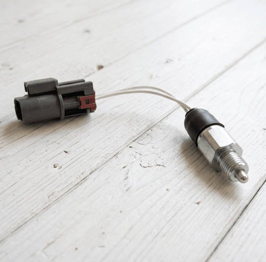 Nissan R33 Skyline manual reverse light switch with grey connector, wires, and metallic threaded sensor on wood.