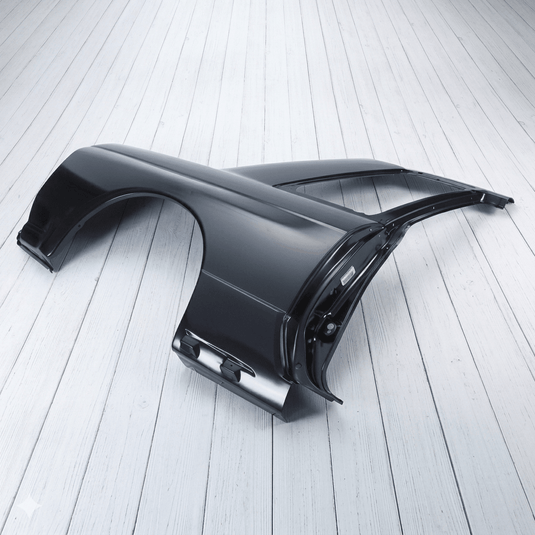 Black Nissan R32 GTR right-hand side quarter panel assembly, brand new Heritage part on a white wooden floor.