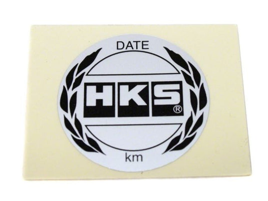 White HKS oil filter service reminder sticker for Nissan and Toyota models, featuring black logo and text.