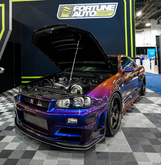 Car with open hood at a car show, Fortune Auto Performance banner in the background