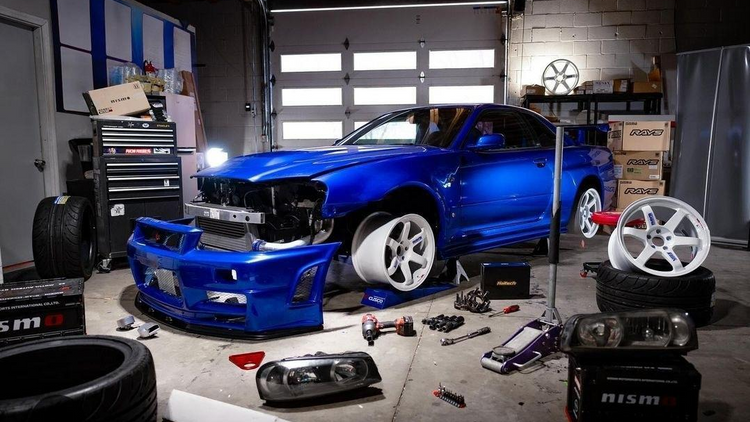 Blue car with visible damage in a garage with tools and parts scattered around.