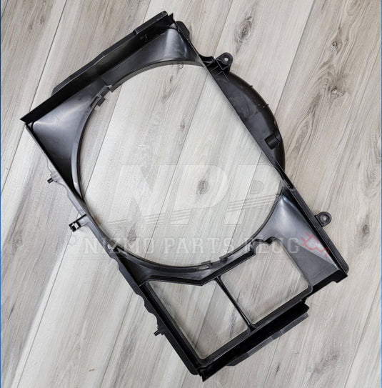 Black plastic radiator fan shroud for Nissan R34 Skyline GTT in good condition, shown against a wood floor background.