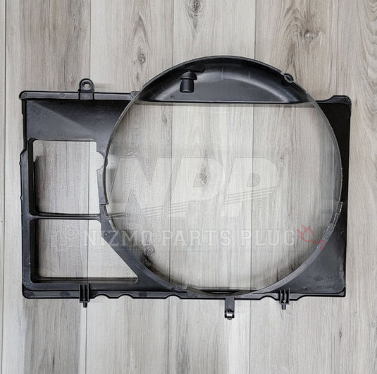 Black Nissan R34 Skyline GTT radiator fan shroud in good condition on a wood grain background.