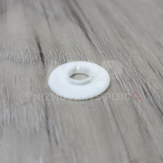 White plastic fender washer for Nissan R34 Skyline GTR on a wood grain background.