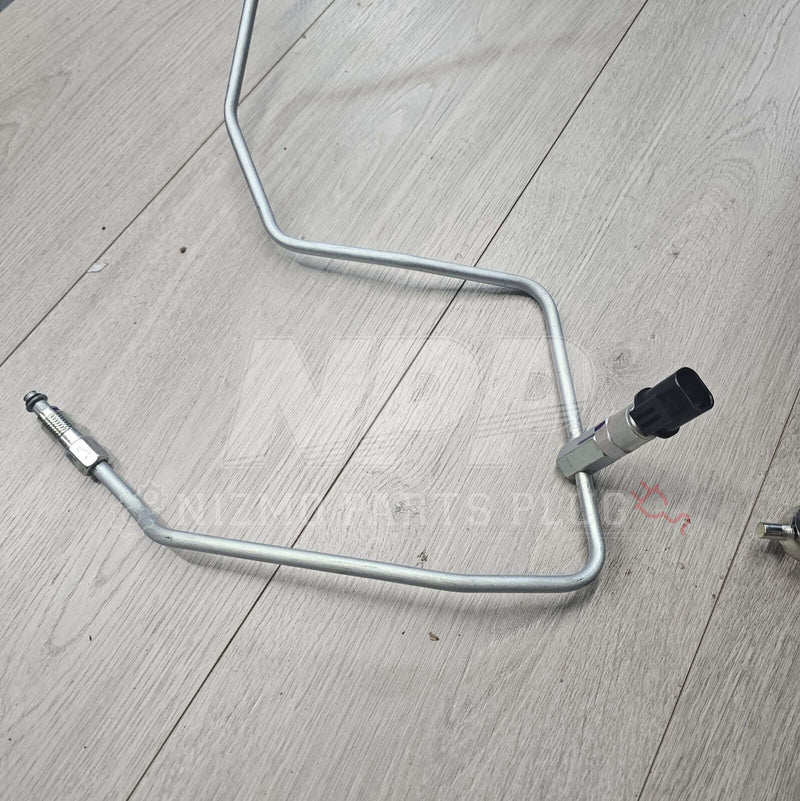 Load image into Gallery viewer, Nissan R34 Skyline high-pressure power steering tube in silver metal with black sensor fitting on wood background.
