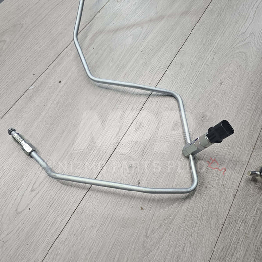 Nissan R34 Skyline high-pressure power steering tube in silver metal with black sensor fitting on wood background.