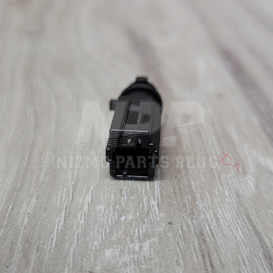 Black Nissan R34 Skyline glove box light connector, shown from the front on a light wood surface.