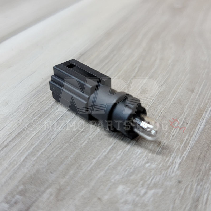 Cargue la imagen en el visor de la galería, Black Nissan R34 Skyline glove box light connector with integrated bulb, shown on a wood grain background.
