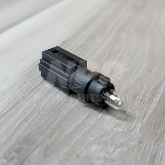 Black Nissan R34 Skyline glove box light connector with integrated bulb, shown on a wood grain background.