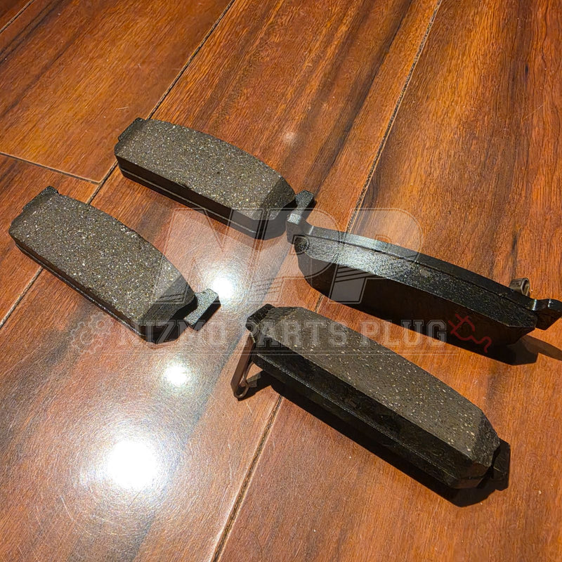 Load image into Gallery viewer, Four used black rear brake pads for a Nissan Stagea RS4-V, laid out on a wooden floor.

