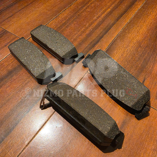 New Nissan Stagea RS4-V rear brake pads. Four dark grey pads with metallic texture on a wooden floor.