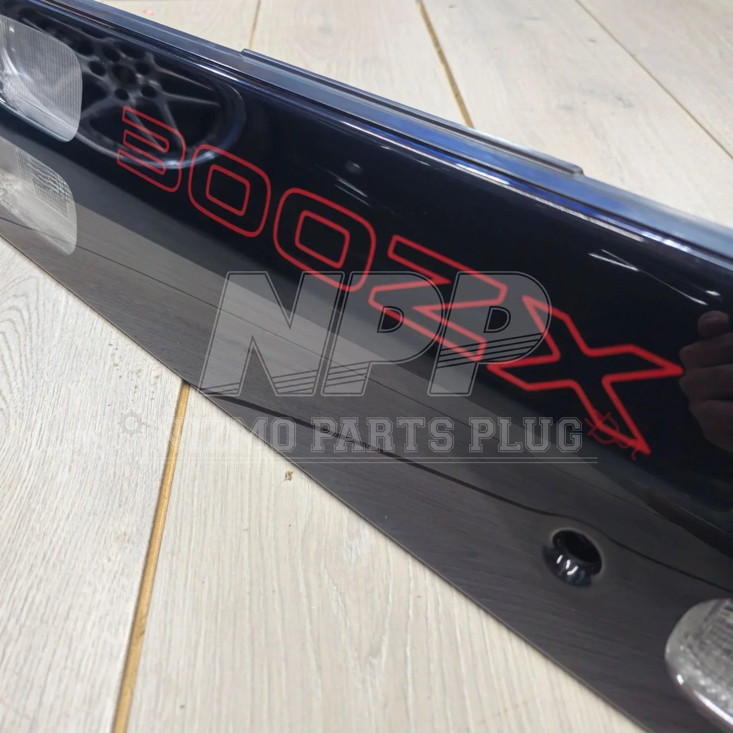 Nissan 300ZX rear tail light panel with red lettering on a wood floor