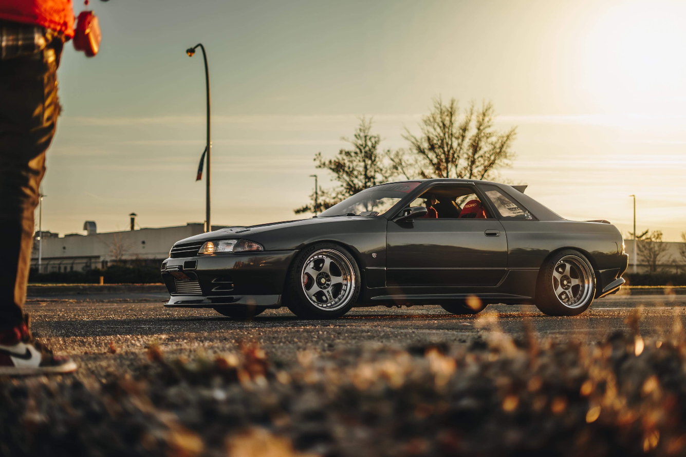Black sports car parked on a road with a person partially visible on the left.